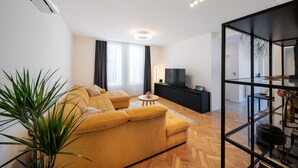 A modern living room with a sofa set, a TV, and a glass partition with decorative items.