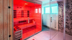 A sauna room with a glass door, wooden benches, and a small table with a bowl and a brush.