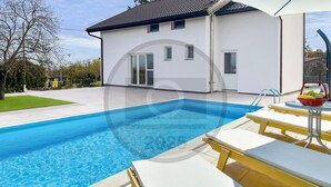 A modern house with a swimming pool, a patio with lounge chairs, and a garden.