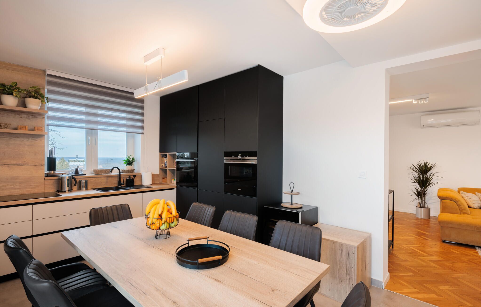 Eine moderne Küche mit schwarzen Schränken, einem Holztisch und Blick auf die Stadt durch große Fenster.