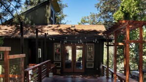 A wooden deck with a pergola and benches, leading to a building with a glass door and windows.