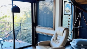 A modern living room with a large window, a leather armchair, a small ottoman, and a view of the outdoors.