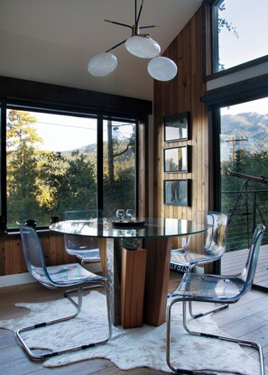 Un comedor moderno con una mesa y sillas de vidrio, detalles de madera y grandes ventanales con vistas al exterior.