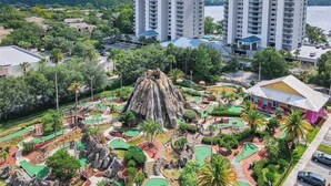 A resort with a central rock formation, multiple swimming pools, and high-rise buildings in the background. - Lake View Resort, 2 BR, 2 bath, sleeps 8, 2 MI to Disney with pool, balcony, gym (Orlando)