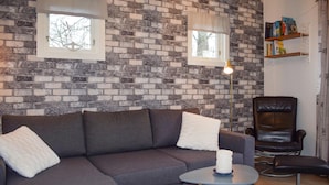 Un salon avec un canapé gris, une table basse ronde, un fauteuil en cuir noir et un mur en briques.