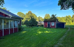 A red building with a covered porch, a small shed, and a well-maintained lawn. - Cozy home in Lidhult with house a panoramic view (Lidhult)