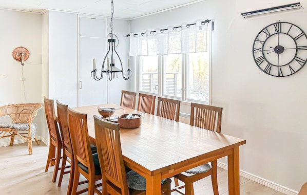 Un comedor con mesa y sillas de madera, una lámpara de araña y un gran reloj de pared.