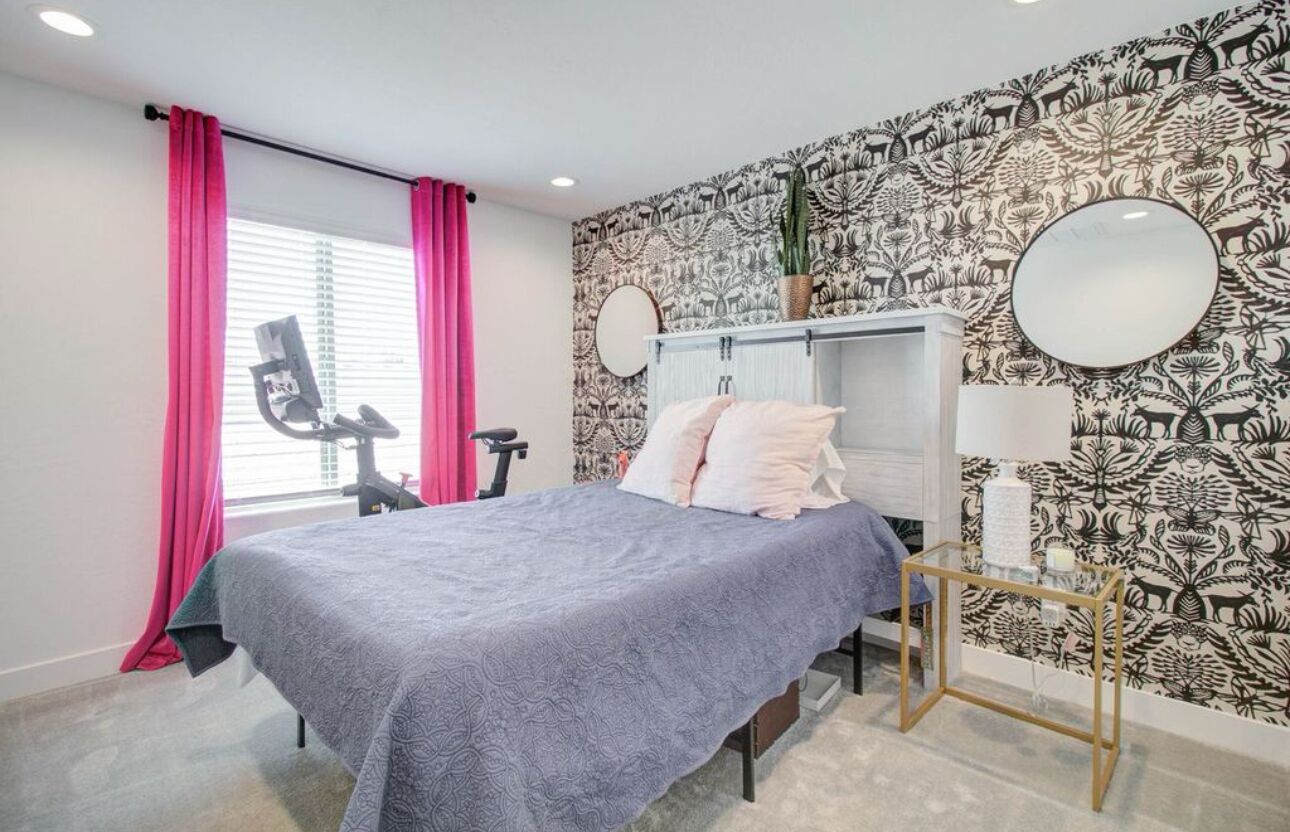 Ein Schlafzimmer mit einem Bett, einem Schreibtisch, einem Stuhl, einem Spiegel und einer Wand mit floralem Muster.