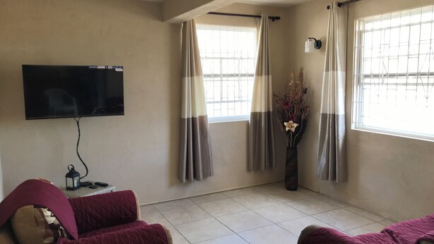A living room with a flat-screen TV, two sofas, a ceiling fan, and a window with curtains. - TRINITY BREEZE APARTMENT 1 (Christ Church)
