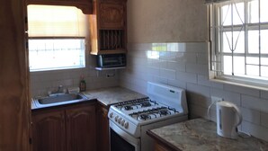 A kitchen with wooden cabinets, a built-in microwave, a gas stove, and a window with blinds. - TRINITY BREEZE APARTMENT 1 (Christ Church)