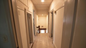 Un pasillo estrecho con piso de madera y paredes blancas, que conduce a una señal de salida al final.
