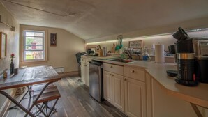 Cocina con armarios de madera, lavavajillas, fregadero y ventana con vista a una casa.