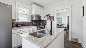A modern kitchen with white cabinets, a granite countertop, stainless steel sink, and a built-in oven. - Family Getaway Near Zoo & Downtown Fun! Sleeps 10 (Atlanta)