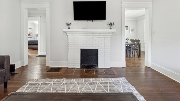 A living room with a white fireplace, a flat-screen TV mounted above it, and a patterned rug on the floor. - Family Getaway Near Zoo & Downtown Fun! Sleeps 10 (Atlanta)
