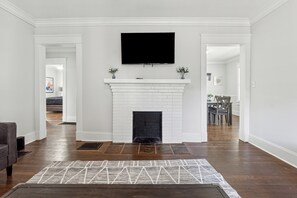 A living room with a white fireplace, a flat-screen TV mounted above it, and a patterned rug on the floor. - Family Getaway Near Zoo & Downtown Fun! Sleeps 10 (Atlanta)
