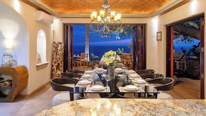 A dining area with a large table set for six, a chandelier, and a view of the ocean.