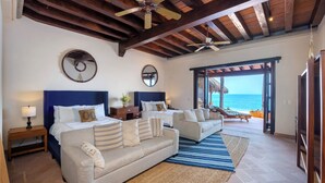 A spacious bedroom with a large bed, two bedside tables, a sofa, and a view of the ocean.