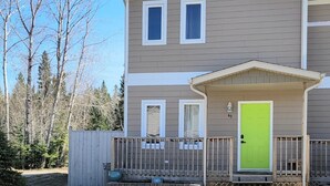 A two-story building with a green door, a covered porch, and a number '49' on the front wall. - Candle Lake retreat backing the 5th green of the golf course. (Candle Lake)