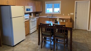 A compact kitchen with wooden cabinets, a white refrigerator, a microwave, a stove, and a dining table with chairs. - Candle Lake retreat backing the 5th green of the golf course. (Candle Lake)