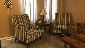 A living room with two striped armchairs, a small table with a lamp, and a decorative wall hanging. - Candle Lake retreat backing the 5th green of the golf course. (Candle Lake)