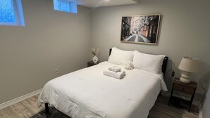 A neatly arranged bedroom with a bed, a bedside table with a lamp, a small vase, and a painting on the wall.