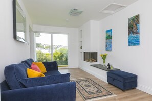 A modern living room with a sofa, ottoman, fireplace, and artwork on the wall.