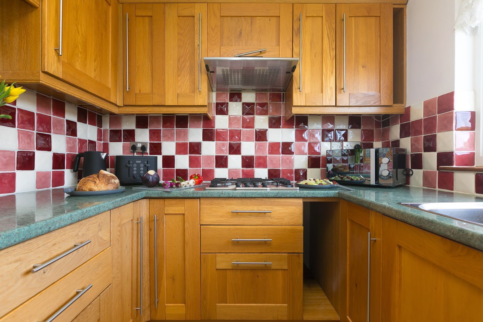 A kitchen with wooden cabinets, a tiled backsplash, a stove, and a toaster.