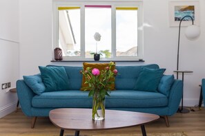 A living room with a teal sofa, a wooden coffee table, and a vase with flowers. - Ocean Parc - Sea Views/Pet Friendly (Carbis Bay)