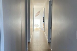 A narrow hallway with a wooden floor leading to a room with a large window.