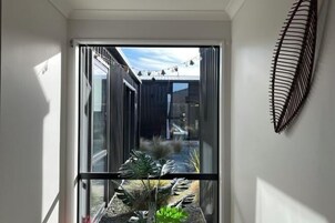 Un interior moderno con una puerta de cristal que da a un espacio exterior, barandilla de metal negro y una lámpara fijada a la pared.