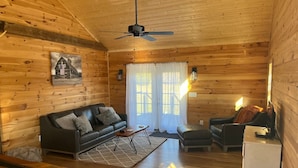 Interior acogedor de una cabaña con techo de madera, ventilador de techo, sofá, mesa de centro, televisor y refrigerador.