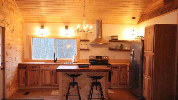 Una cocina de estilo cabaña de madera con una isla central, taburetes de bar, una estufa y un refrigerador.