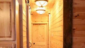 Un pasillo de madera con una puerta al final, un accesorio de iluminación en el techo y suelo de madera.