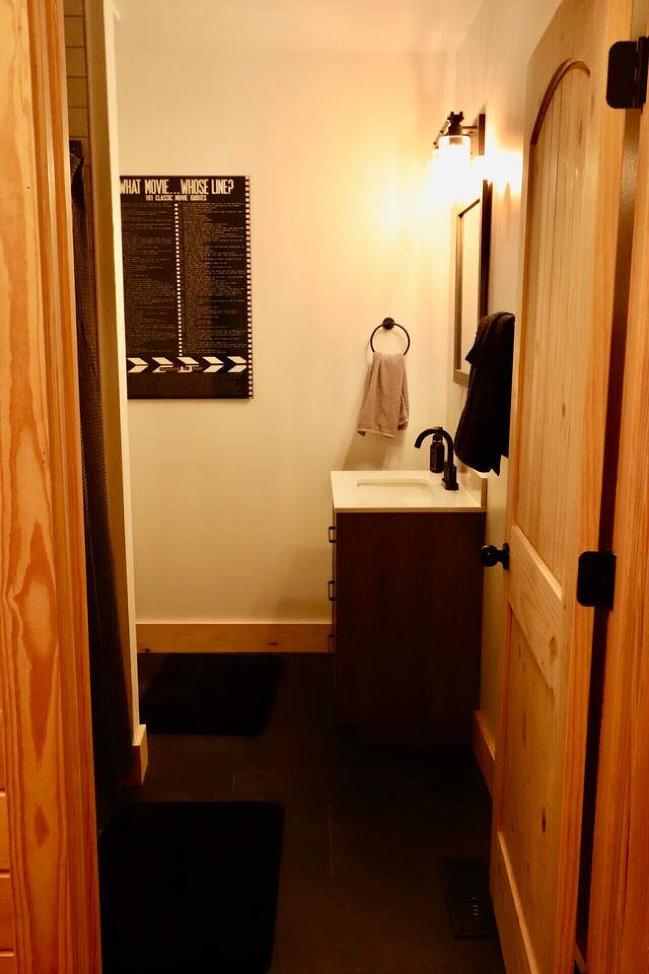 A narrow bathroom with a wooden door, a white sink, a towel rack, and a poster on the wall.