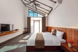 Una habitación de hotel con una cama, televisión, cabecero de madera, mesita de noche y ventana con cortinas.