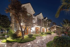 A two-story house with a stone pathway leading to the entrance, surrounded by well-maintained greenery and palm trees. - La Vento Resort Ninh Binh (Tay Hoa Lu)