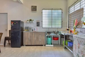 A compact kitchen with a refrigerator, microwave, and sink. There is a window with a grid pattern, and a door on the left. - NewWALAI N3 Landed house near IMAGO KK CarGarage (Kota Kinabalu)