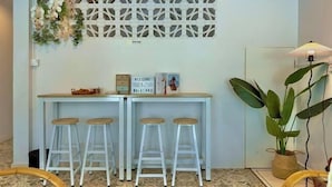 Zona de recepción con escritorio blanco, dos taburetes, un panel decorativo y una planta en maceta.