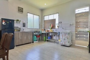 A kitchen with a refrigerator, microwave, and wooden cabinets. There are two windows with metal bars and a door with a glass panel. - NewWALAI N3 Landed house near IMAGO KK CarGarage (Kota Kinabalu)