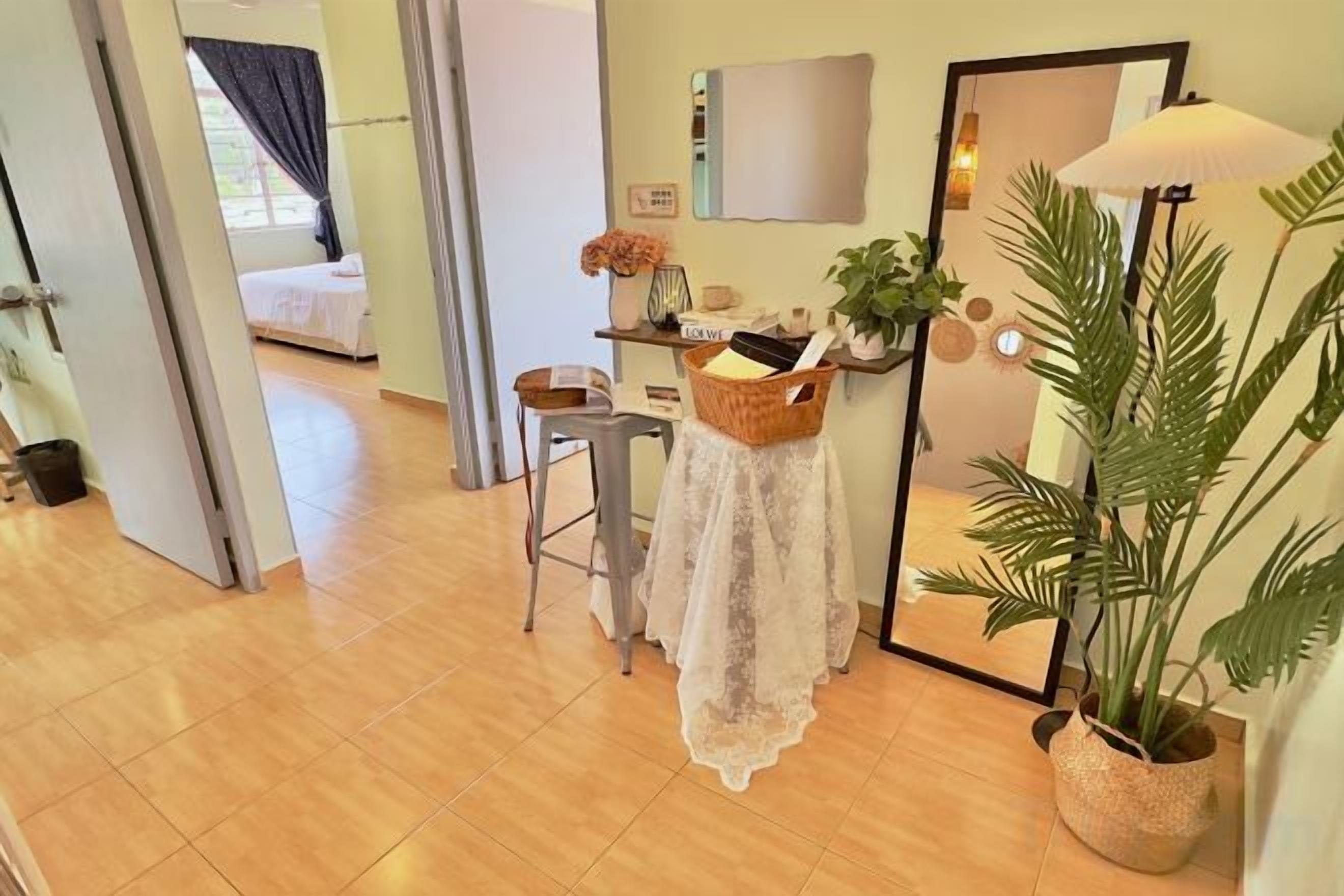 A hotel room with a bed, a desk with a lamp, a mirror, and a potted plant.