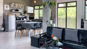 A modern kitchen with white cabinets, a dining table, and chairs. There is a black leather sofa and a small table with a vase of flowers. - Silpasom ARTstay Suratthani (Phunphin)