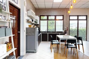 A kitchen with a dining table and chairs, a refrigerator, and a window with a view. - Silpasom ARTstay Suratthani (Phunphin)