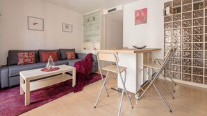 Ein modernes Wohnzimmer mit grauem Sofa, einem Holztisch, einem roten Teppich, einem Schreibtisch mit Stuhl und einer Wand mit Spiegel und Kunstwerken.