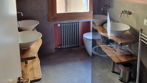 Ein rustikales Badezimmer mit freiliegenden Holzbalken, einem Fenster, einer Heizung und einem Holzwaschtisch mit einer Schüsselspüle.