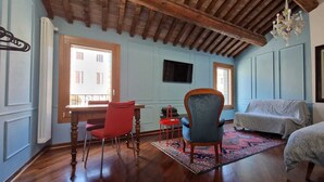 Ein Zimmer mit Holzboden, ein roter Stuhl, ein blauer Sessel, eine Couch, ein Teppich mit Muster und ein Gemälde an der Wand.