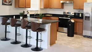 Una cocina moderna con armarios de madera, una isla central con taburetes de bar, un refrigerador de acero inoxidable y un microondas.