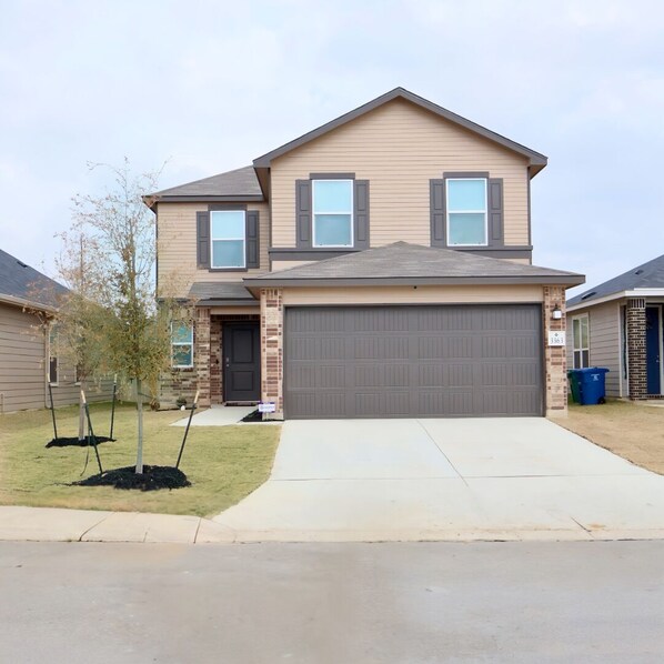 A two-story house with a garage, a front yard with young trees, and a clear sky.