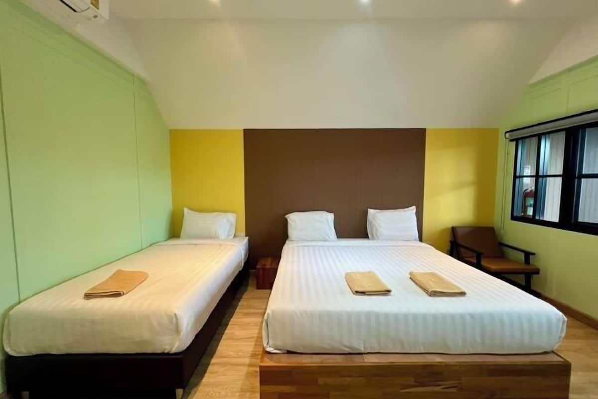 A hotel room with two single beds, a wooden floor, a window with blinds, and a green wall.
