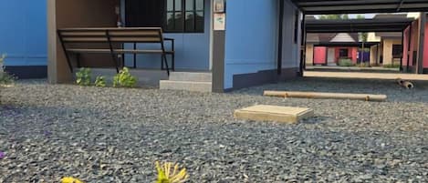 A building with a covered entrance, a bench, and a gravel ground.