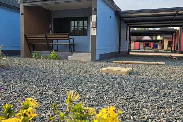 A building with a covered entrance, a bench, and a gravel ground.